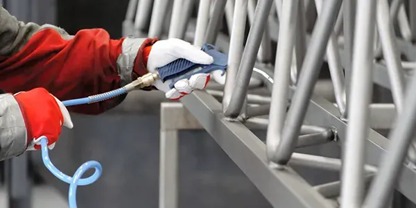 Worker removing abrasive from part using pressurised air